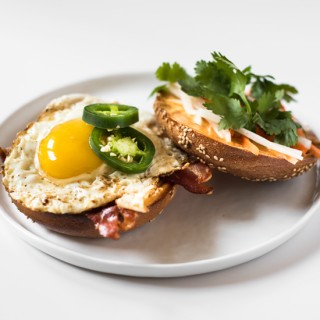 This Breakfast Bánh Mì is a bagel topped with bacon, a fried egg, Sriracha-mayo, do chua, sliced jalapeno, and cilantro. Bring lots of napkins!